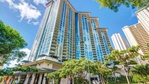 A high-rise hotel with multiple floors, large windows, and a well-maintained garden area with trees and shrubs. - Deluxe 2BR Condo in Waikiki! (Honolulu)