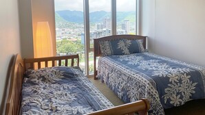 A bedroom with two beds, large windows, and a view of a cityscape. - Deluxe 2BR Condo in Waikiki! (Honolulu)