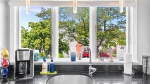 Una cocina con un ventanal grande, una cafetera, un lavabo y diversos utensilios de cocina sobre la encimera.