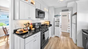 Una cocina moderna con armarios blancos, una estufa negra y un microondas. Hay una isla de madera con utensilios de cocina y un hervidor. Se ve un cartel con la palabra 'welcome' en la pared.