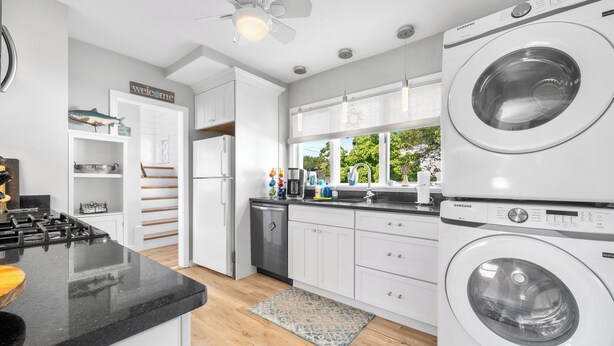 Una cocina moderna con armarios blancos, encimera negra, estufa integrada, lavavajillas y una lavadora Samsung.