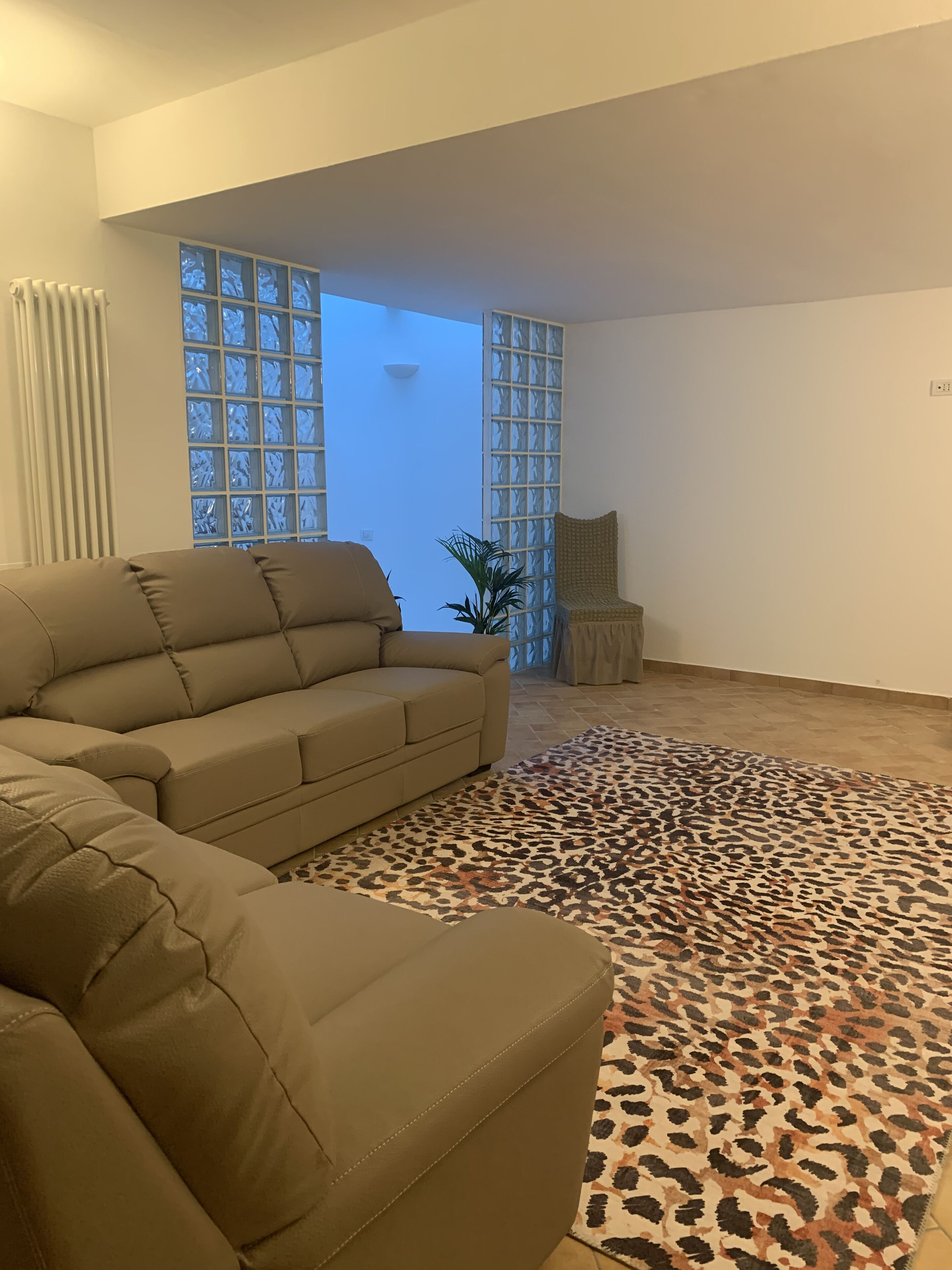 Un salon avec un canapé d’angle, un tapis à motifs léopard et une vue sur l’extérieur, accessible par une porte vitrée.