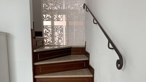 A staircase with wooden steps and a metal handrail, leading to a room with a white wall and a decorative window.