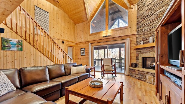 Un salón espacioso con una escalera de madera, una chimenea de piedra y un ventanal grande.