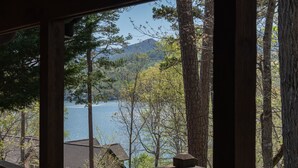 Vista a través de una ventana de una cabaña con vista a un lago rodeado de árboles y una montaña.