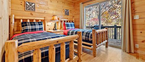 Una cabaña de madera con dos camas, una ventana que da a un paisaje de árboles, y una terraza de madera en el exterior.