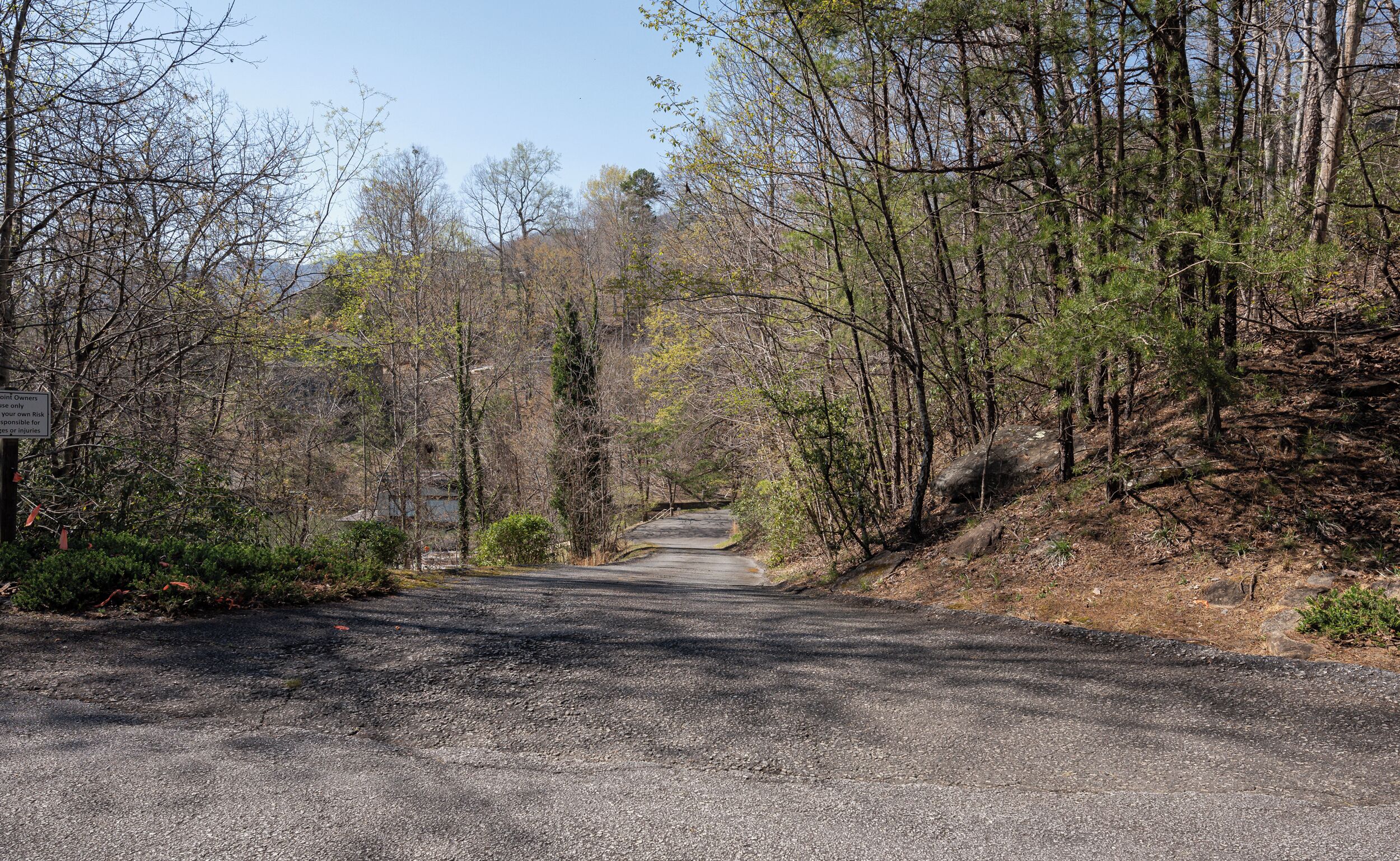 A gravel road leading through a forested area with a sign warning about point owners' liability.