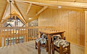 A wooden interior with a high ceiling, a stone wall, and a view through a window.
