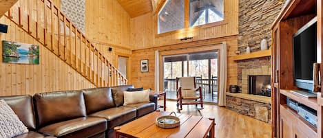 Un salón espacioso con una escalera de madera, una chimenea de piedra y un ventanal grande.