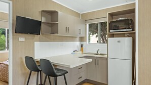A modern kitchen with a flat-screen TV mounted above the counter, a microwave, and a refrigerator. There are two bar stools and a window providing natural light. - Discovery Parks - Ayr (Ayr)