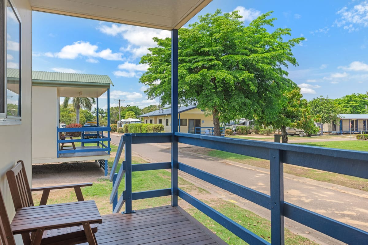 A covered outdoor area with a wooden bench and picnic table, a blue railing, and a view of a street with parked cars and buildings.