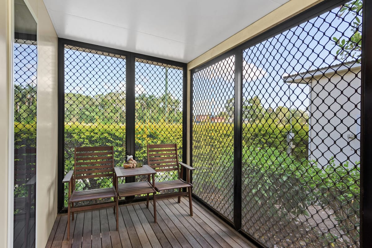 A covered outdoor seating area with a table and two chairs, surrounded by a mesh fence.