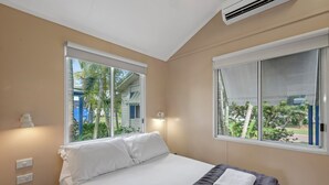 A hotel room with a bed, two windows, a wall-mounted air conditioner, and a small shelf with a lamp. - Discovery Parks - Ayr (Ayr)