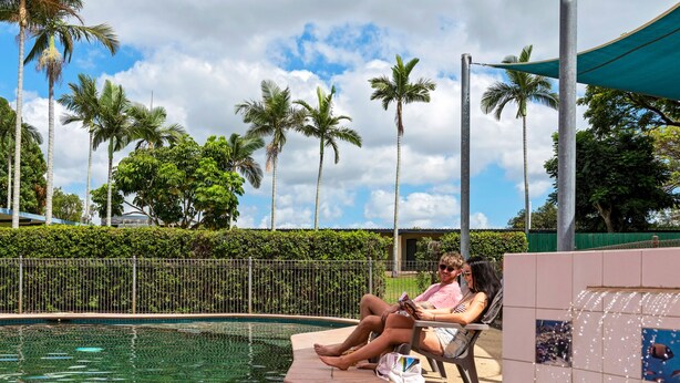 A poolside area with a tiled edge, palm trees, and a metal fence. - Discovery Parks - Ayr (Ayr)