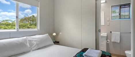 A hotel room with a bed, a window with a view of trees, a bathroom with a toilet and sink, and a towel rack.