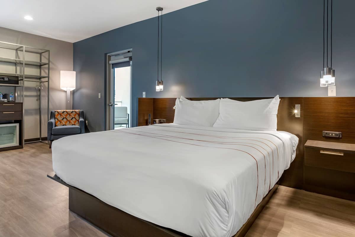 A modern hotel room with a large bed, a desk, a chair, and a view of the outdoors.