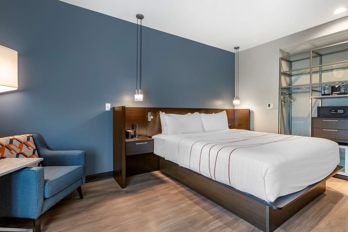 Moderni hotellihuone, jossa on suuri sänky, yöpöytä, tuoli ja seinään upotettu TV-taso.