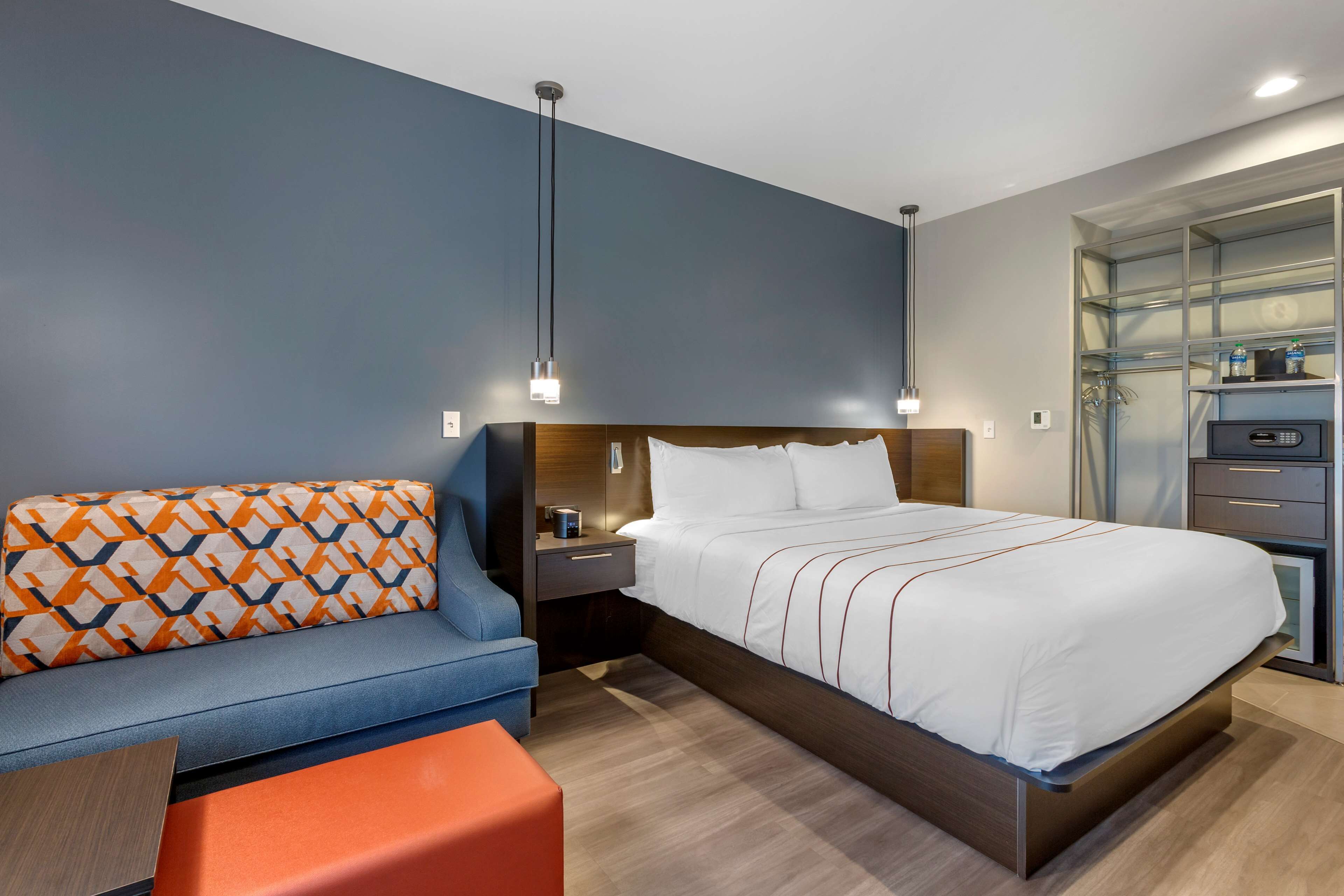 Ein modernes Hotelzimmer mit Bett, Sofa, Nachttisch und integriertem Kleiderschrank.