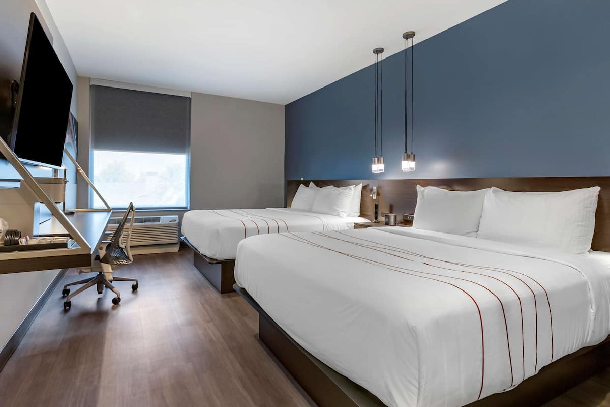 A hotel room with two beds, a desk, a chair, a TV, and a window with a view.