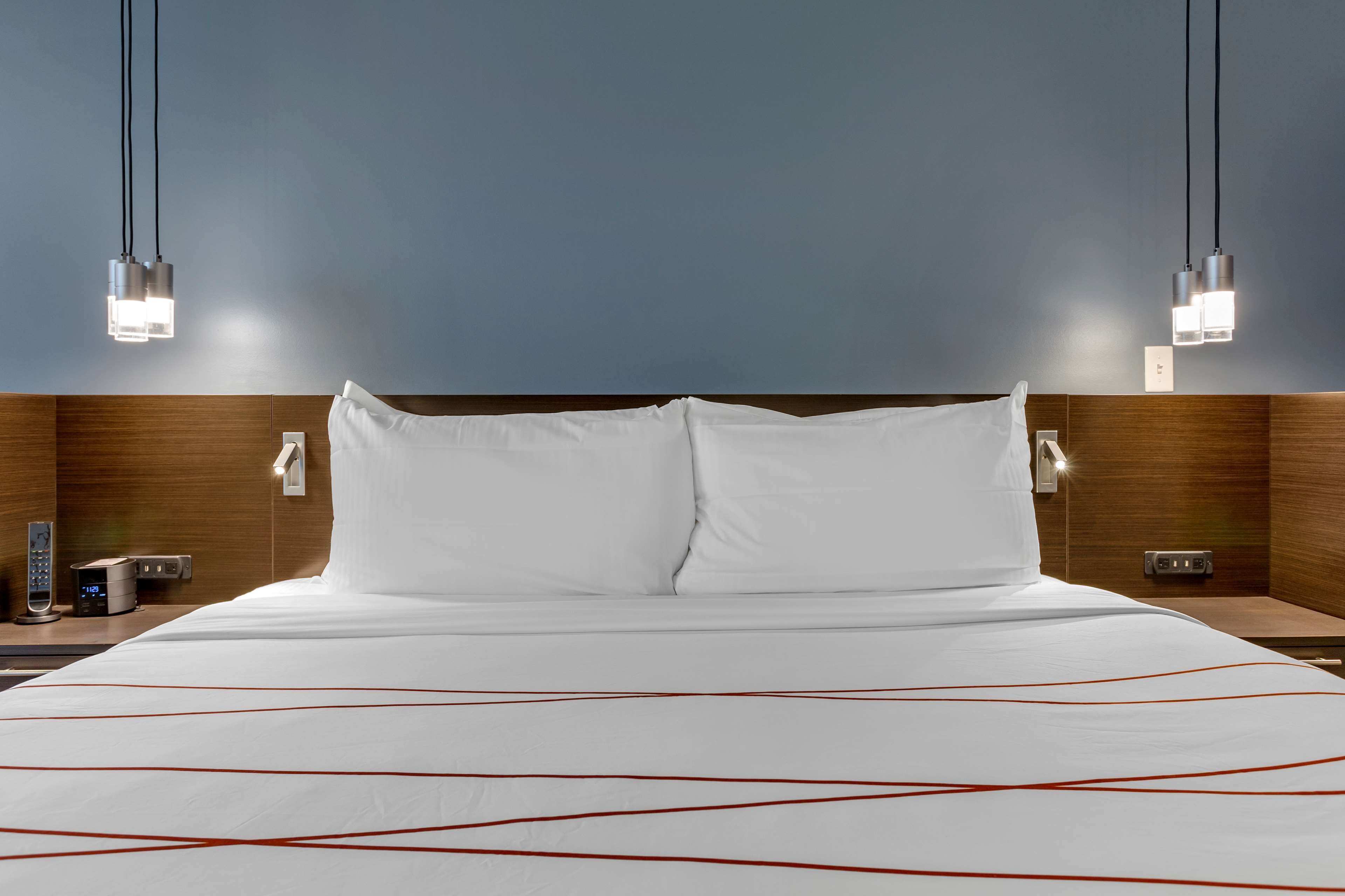 A hotel room with a large bed, wooden headboard, bedside tables, and modern pendant lights.
