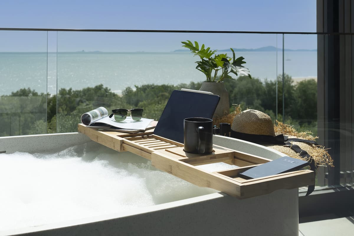 Ein Whirlpool mit Holztischchen, einem Buch, einer Tasse und einer Pflanze auf einem Balkon mit Blick auf ein Gewässer.