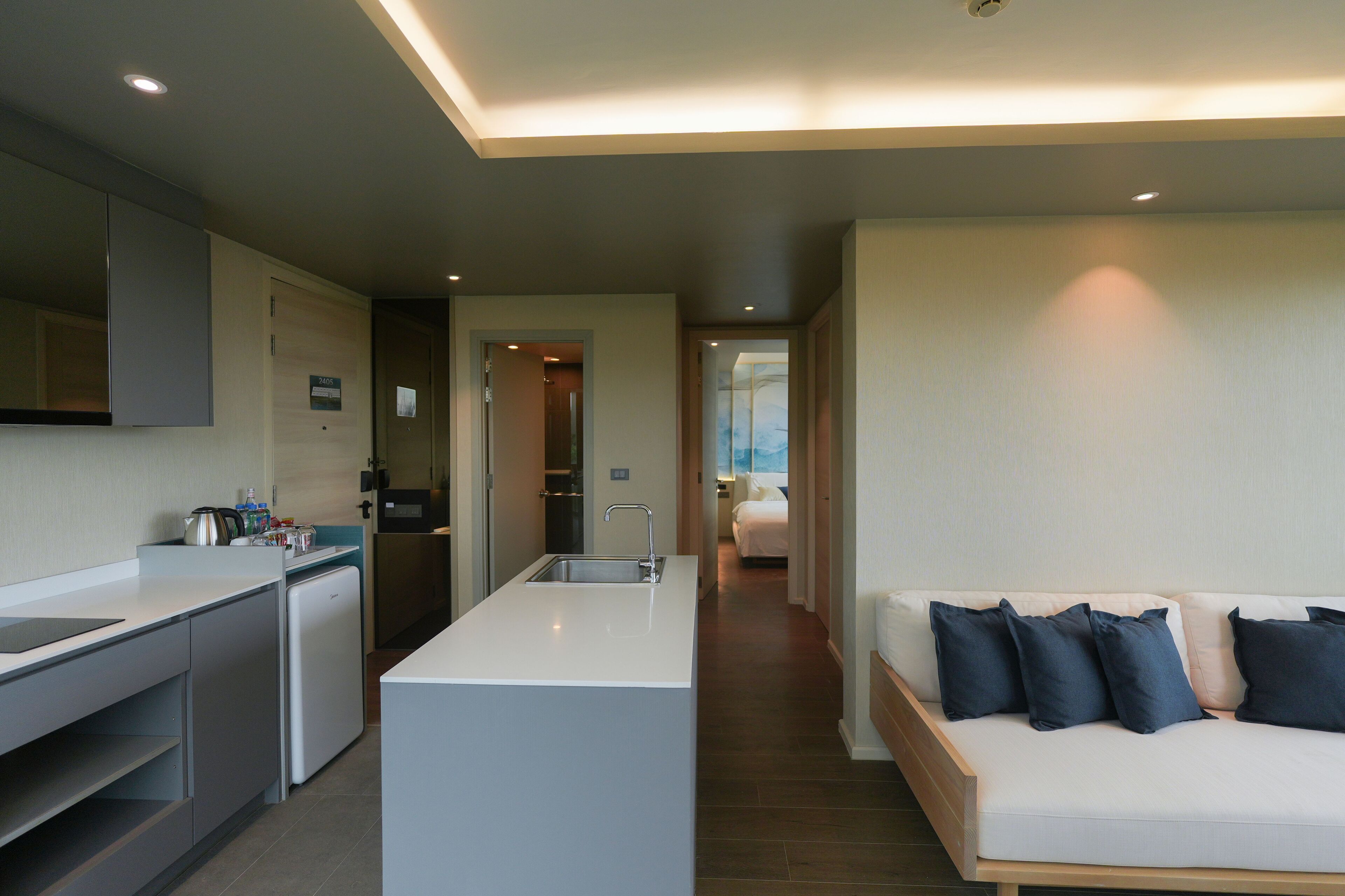 A modern kitchen with a central island, a dining area, and a bedroom with a bed and pillows.