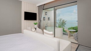 Een moderne slaapkamer met een groot bed, een flatscreen-tv, een balkon met uitzicht op zee en een kleine tafel met stoel.
