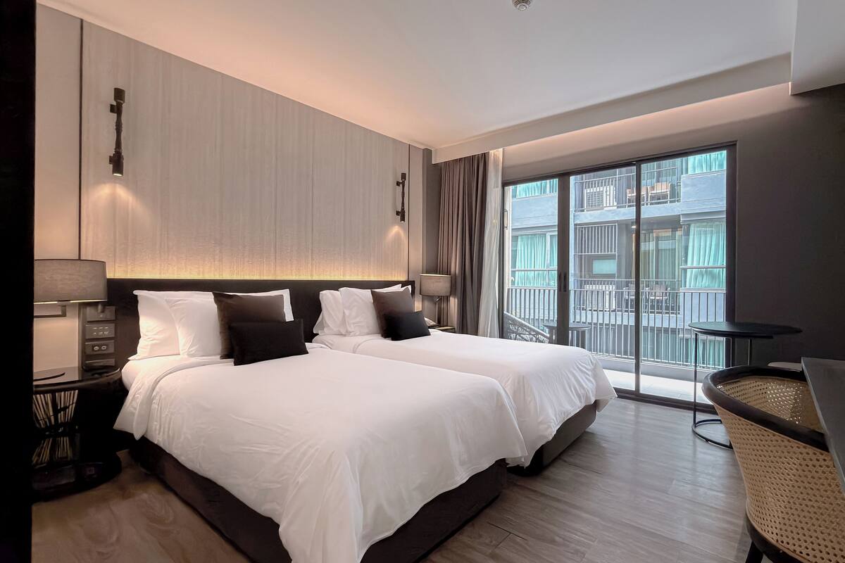 Ein Hotelzimmer mit zwei Betten, einem Balkon, einem Schreibtisch und einem Stuhl.