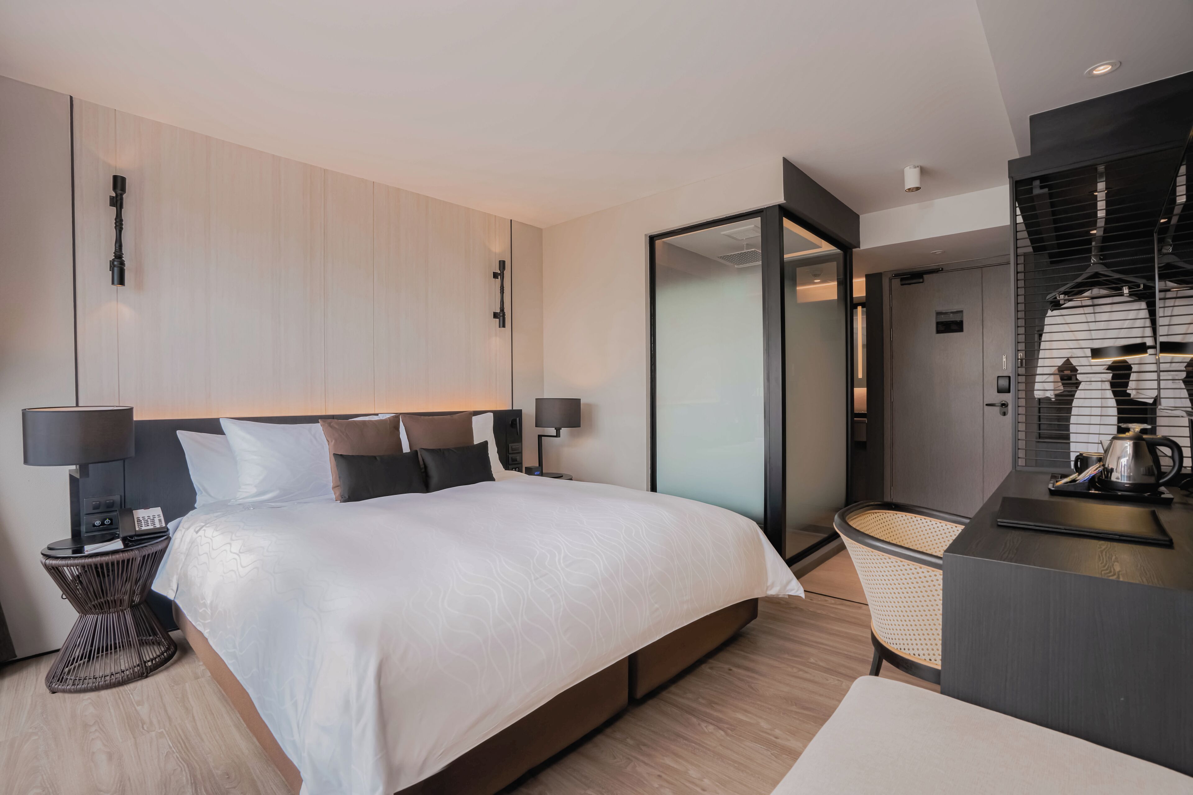Een moderne hotelkamer met een groot bed, bedlampjes, een klein nachtkastje, een bureau met een waterkoker en een stadsgezicht door een glazen deur.