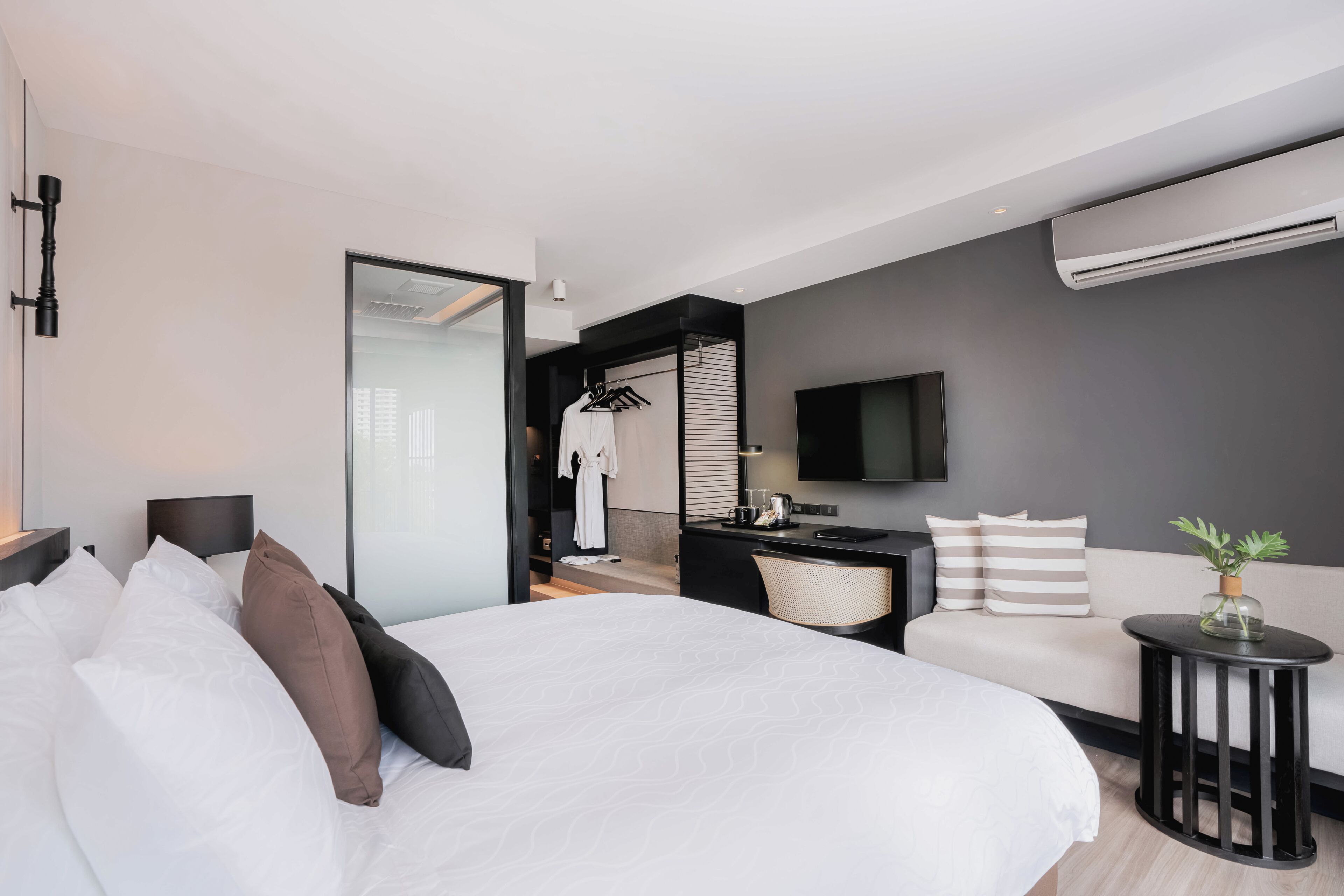 Una habitación de hotel moderna con una cama grande, un sofá, una mesita, un televisor y un equipo de aire acondicionado.