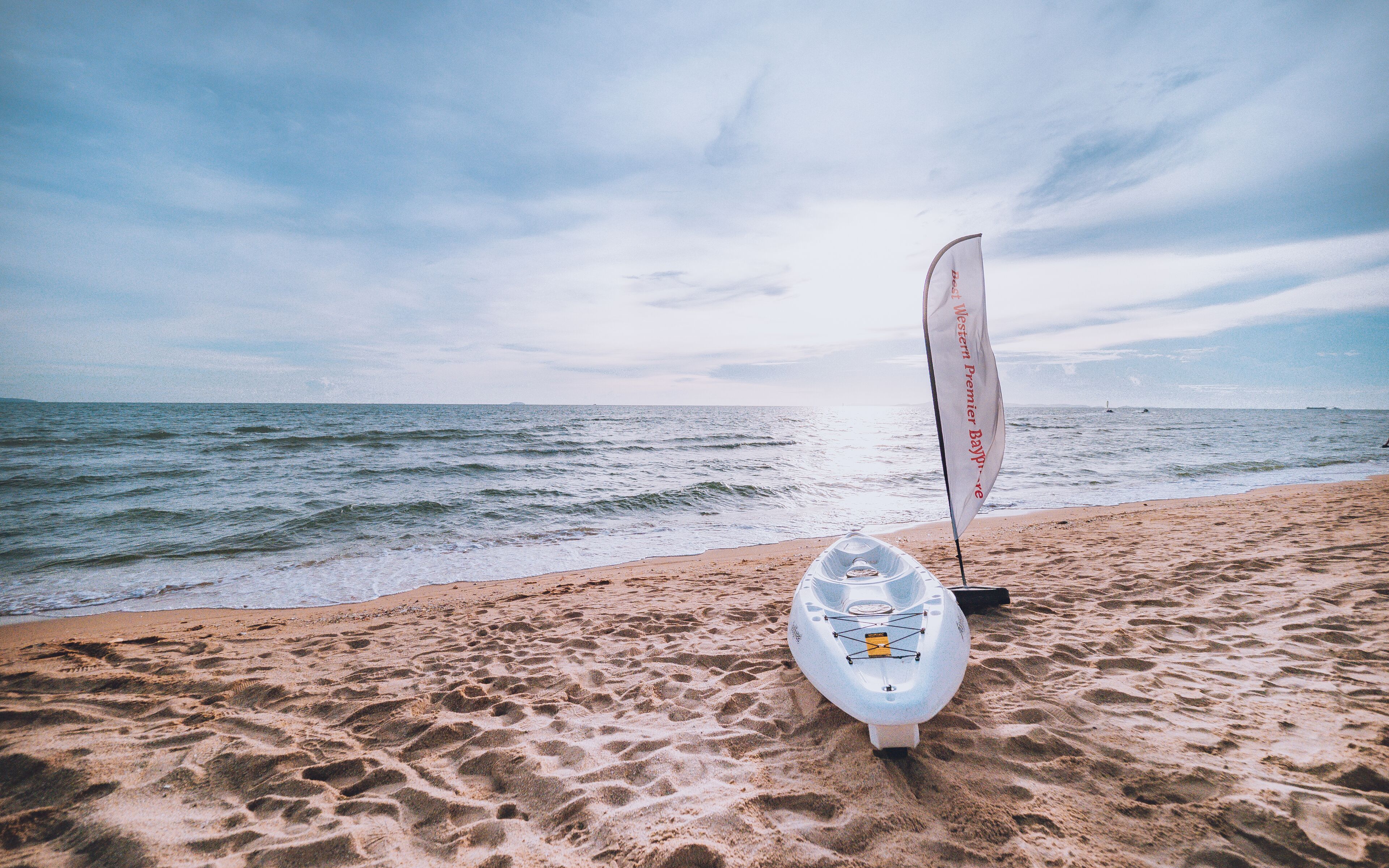 A kayak with a sail on a sandy beach by the sea.
