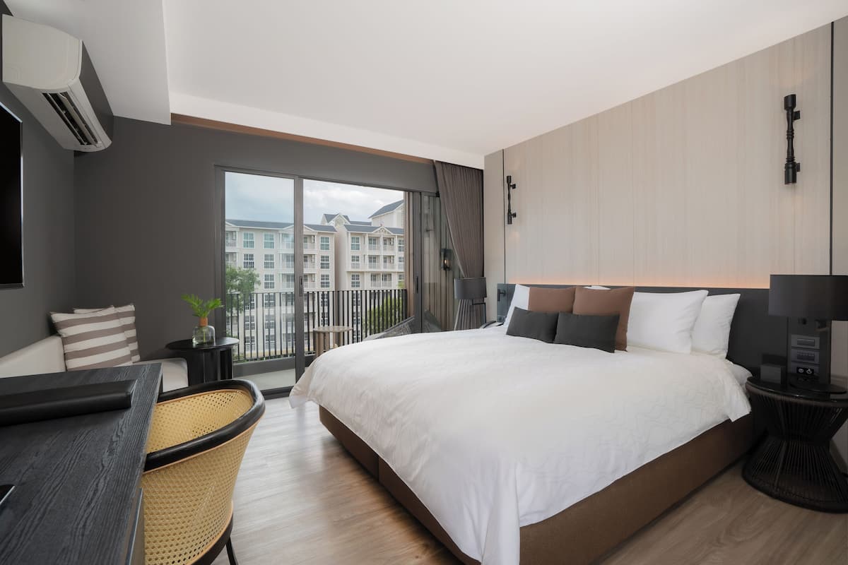 Ein modernes Hotelzimmer mit einem großen Bett, einem Schreibtisch und Blick auf ein Gebäude durch ein großes Fenster.