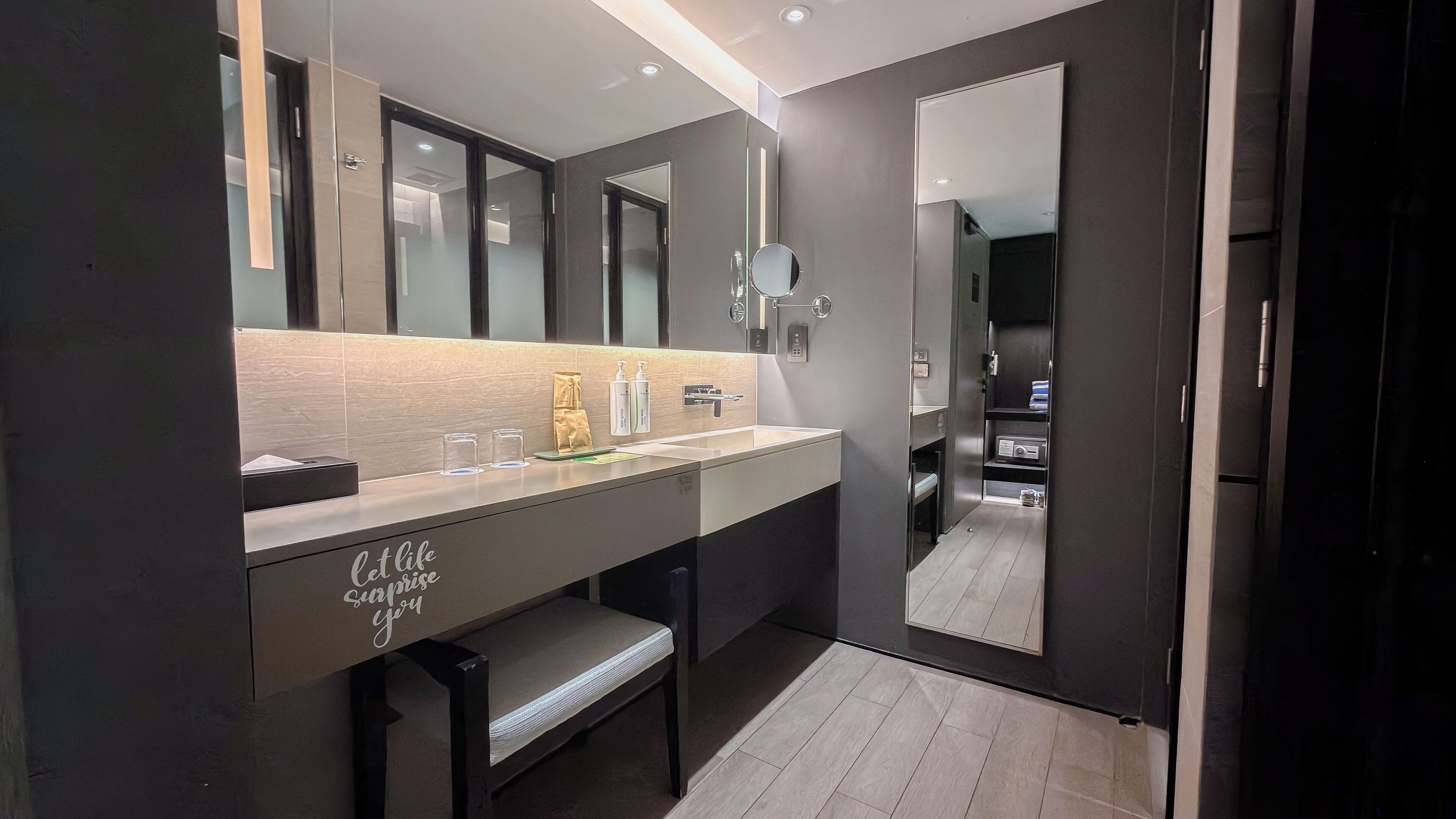 A modern bathroom with a large mirror, a vanity with a countertop, and a bench.