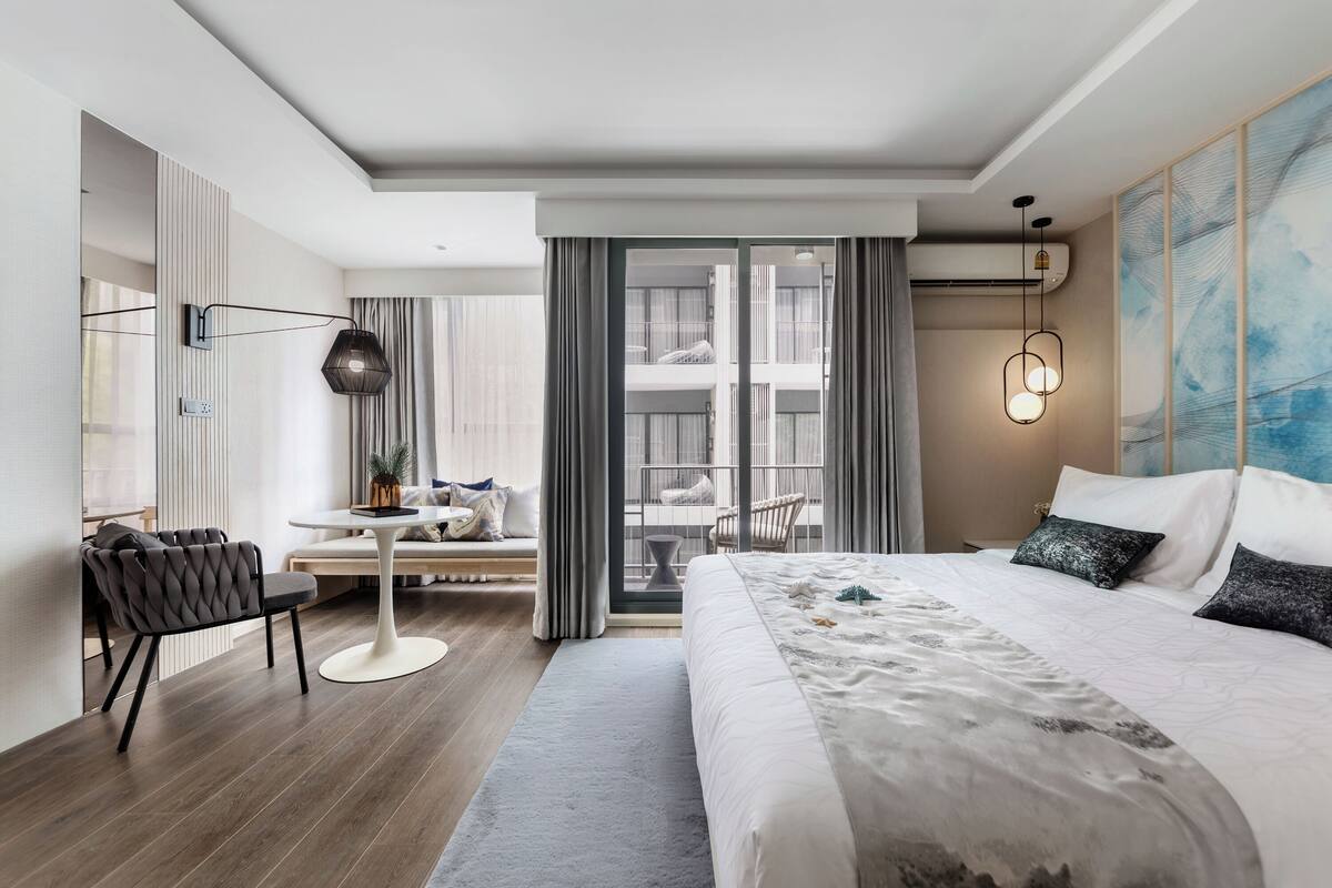 Ein modernes Hotelzimmer mit einem großen Bett, einer Sitzecke mit Tisch und einem Balkon mit Blick.