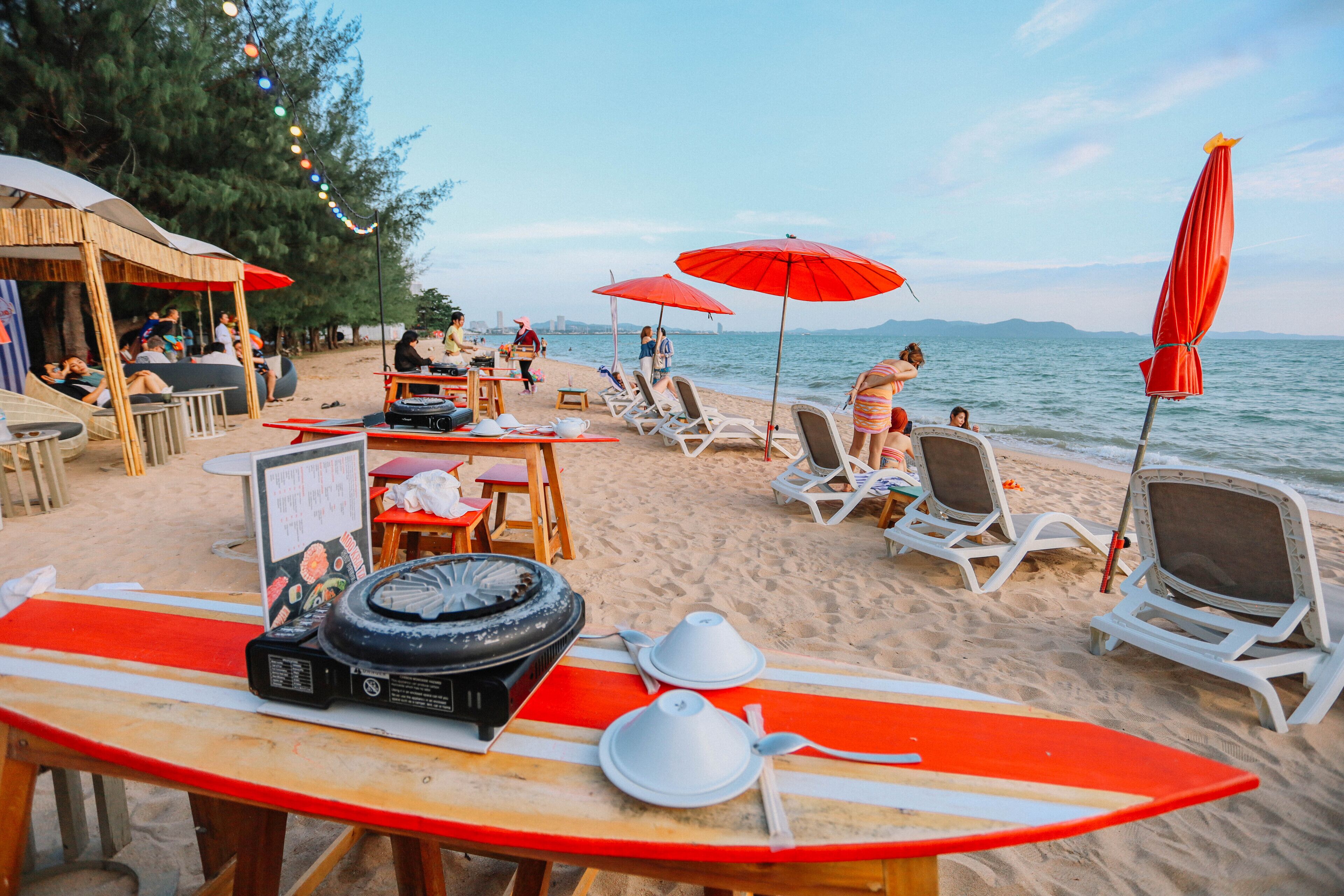 A beachside restaurant with outdoor seating, a surfboard, and a grill.