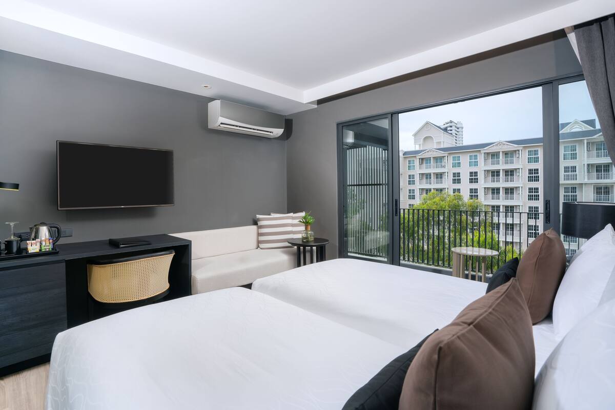 Ein modernes Hotelzimmer mit einem großen Bett, einem Flachbildfernseher, einem kleinen Schreibtisch und einem Balkon mit Stadtblick.