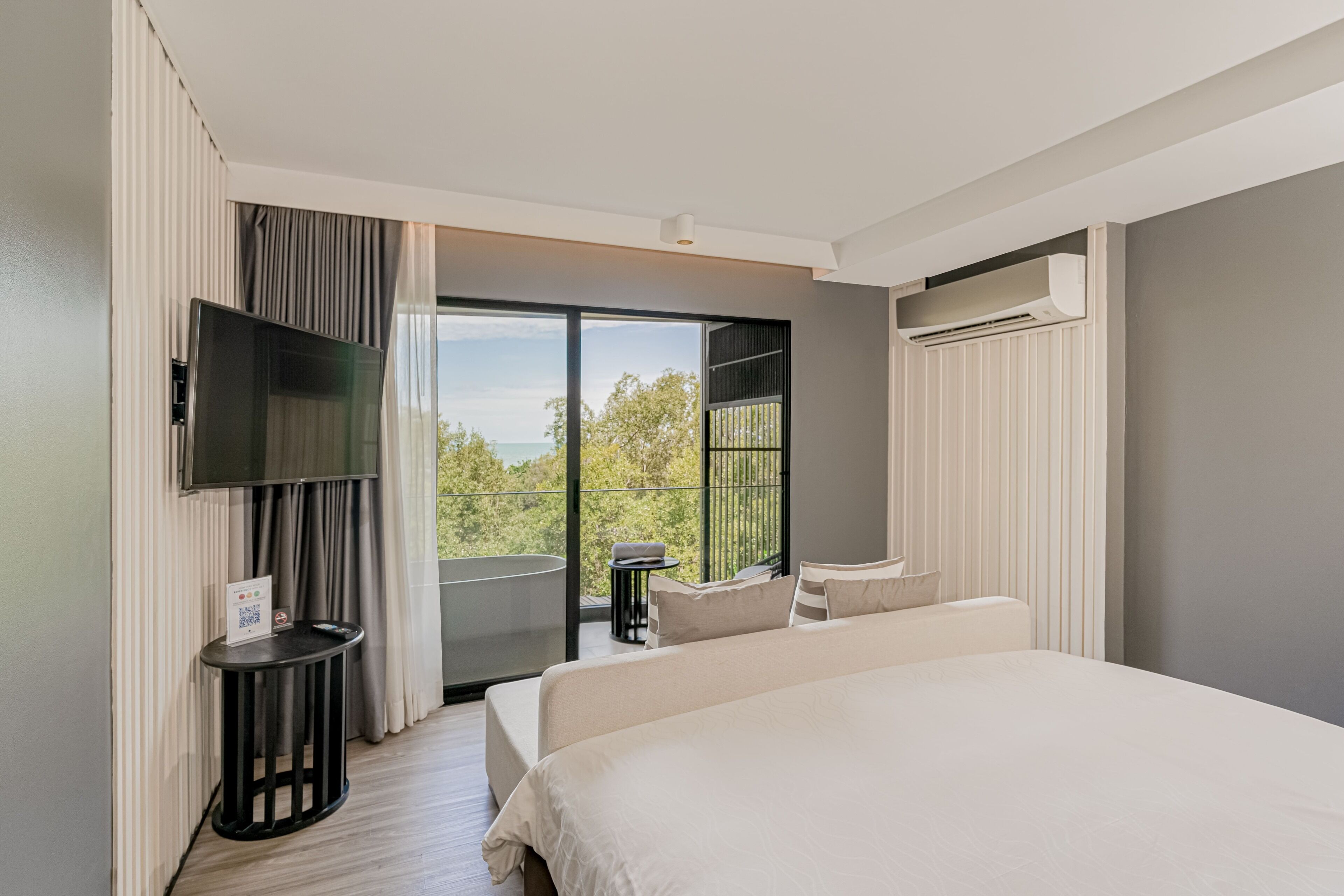A modern hotel room with a large bed, a flat-screen TV, a balcony with a view, and a small table with a chair.