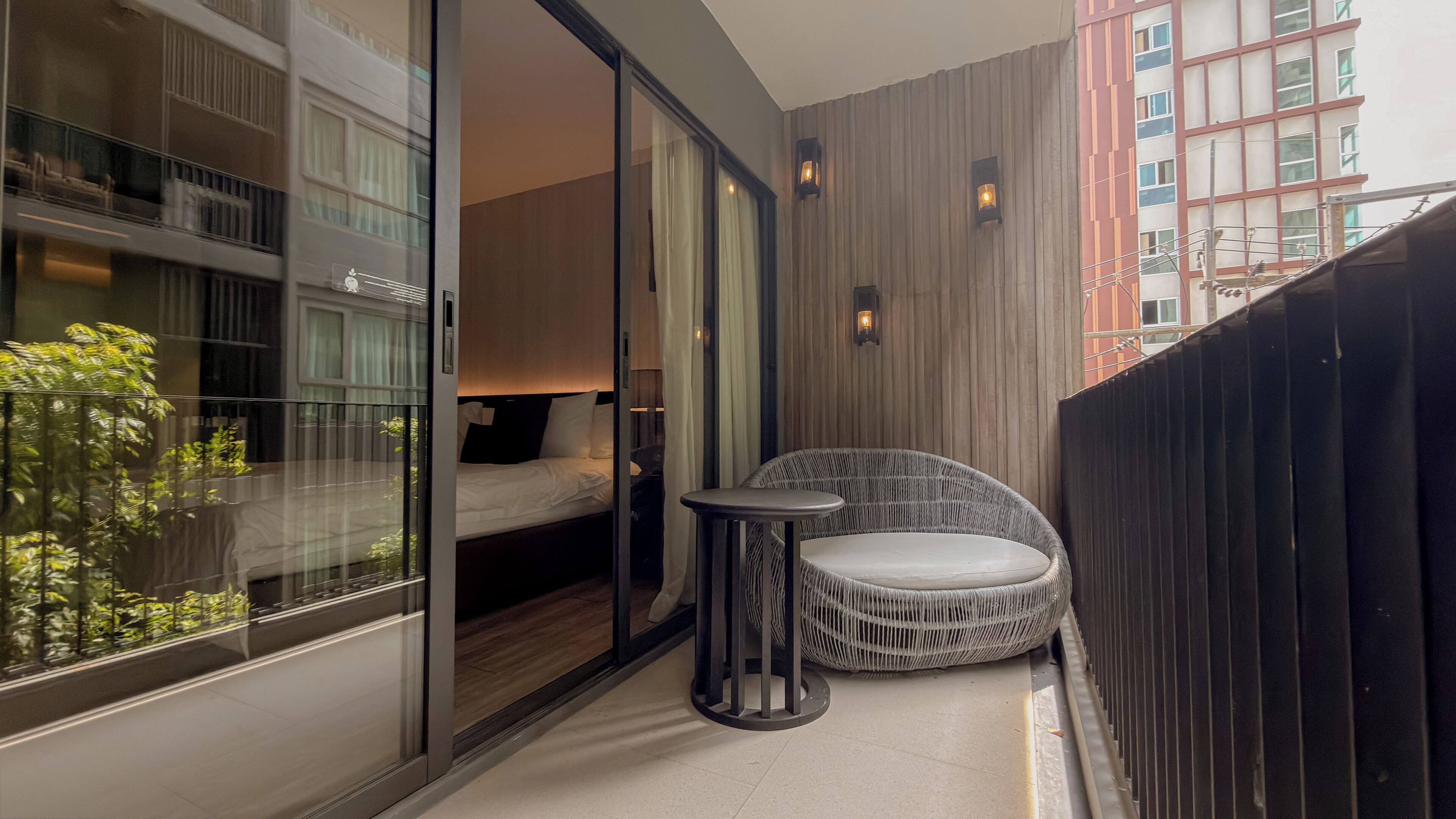 A balcony with a bed, a wicker chair, and a small table.