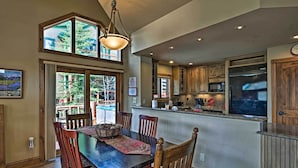 A spacious dining area with a wooden table and chairs, a chandelier, and large windows offering views of the outdoors. - Steps to Gondola! Hot Tub Haven in Breckenridge (Breckenridge)