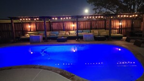 Piscina illuminata da una luce blu, circondata da un solarium in legno e mobili da esterno.