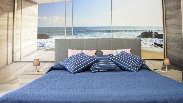 A bedroom with a large window overlooking the ocean, a bed with blue bedding, and two bedside lamps. - SUN SEA HOUSE TAORMINA  (Giardini Naxos)