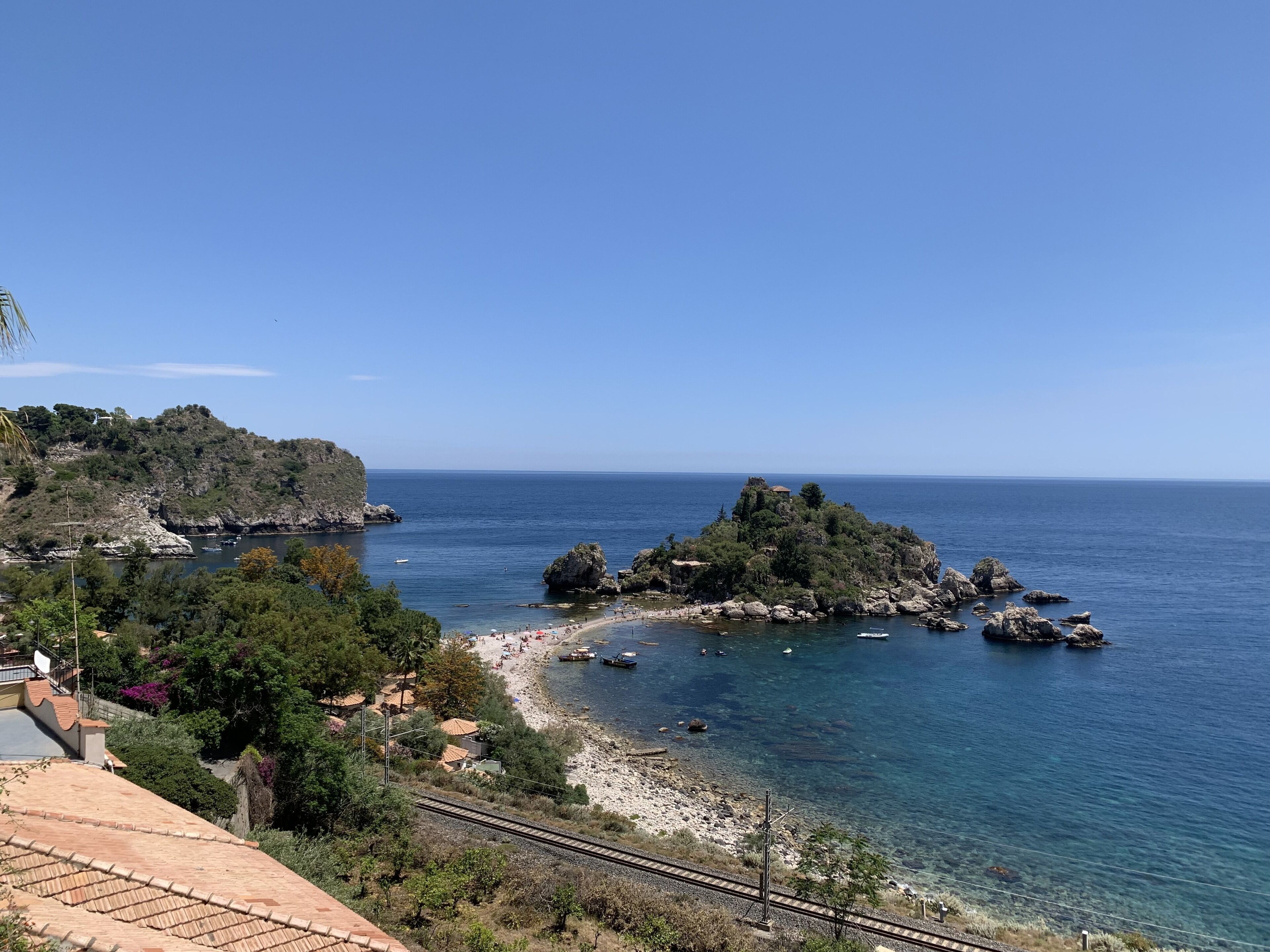 A coastal landscape with a beach, rocky outcrops, and a clear blue sky.