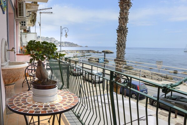 Ein Balkon mit einem Blumentopf, einem Tisch mit Fliesen und Blick auf das Meer und die felsige Küste.