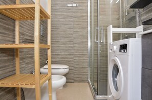 Ein modernes Badezimmer mit integrierter Waschmaschine, einer Duschkabine aus Glas und Holzregalen.