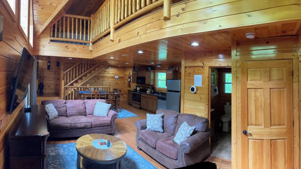 L’intérieur chaleureux de ce chalet comprend un espace de vie avec deux canapés et une table basse, une cuisine équipée d’appareils modernes et un escalier menant à un étage supérieur.