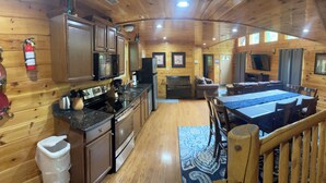 L’intérieur de la cabane est doté de murs en bois, d’une cuisine équipée d’appareils modernes, d’un coin repas avec une grande table et des chaises, ainsi que d’une cheminée.