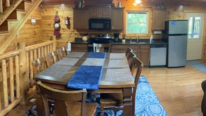 L’intérieur d’un chalet en bois comprend une table à manger, des chaises, un coin cuisine équipé d’appareils électroménagers et un escalier.