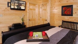 Une pièce en bois avec un lit, un téléviseur fixé au mur et un plateau contenant des livres et des tasses sur le lit.