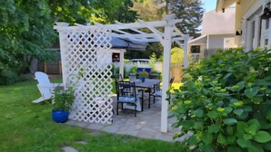 Ein Patio mit einem weißen Pergola aus Gitterholz, Gartenmöbeln und Blumentöpfen.