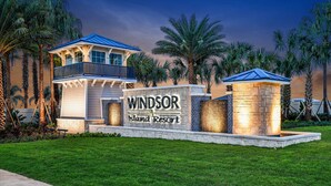 Señal de un resort que dice 'Windsor Island Resort', rodeada de palmeras y un césped cuidado.